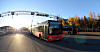 Rød og kremfarget Unibuss på en vei i lav høstsol, med en annen buss og ledninger i bakgrunnen.