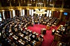 Oversiktsbilde av Stortingets sal med representanter, talerstol og rødt gulv.