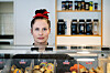 Astri Karine Lundgren bak en kantinedisk med matvarer, drikke og hyller i bakgrunnen.