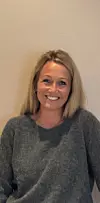 Portrett av Trine Charlotte Ring Voll i grå genser foran en lys vegg.