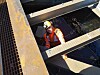 Geir Krokå i oransje verneklær og hjelm mellom stålkonstruksjoner ved et industrielt anlegg.
