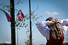 Kvinne i bunad foran norske flagg og blå himmel.