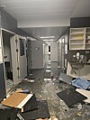 Ødelagt fengselsgang med knust inventar, løse gjenstander og bygningsmaterialer spredt på gulvet.