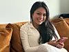 Cinthia Tølche sitter i en brun sofa og holder en rosa mobiltelefon.