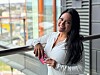 Cinthia Tølche smiler ved et rekkverk i et lyst, moderne glassbygg.