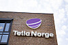 Telia Norge-logo på en rødbrun mursteinsbygning under en lys himmel.