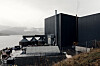 Industrianlegg fra Nordic Mining ved fjorden på Engebø, med mørke bygninger og fjell i bakgrunnen.